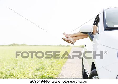 Stock Image - Low section of woman relaxing in car on country road. Fotosearch