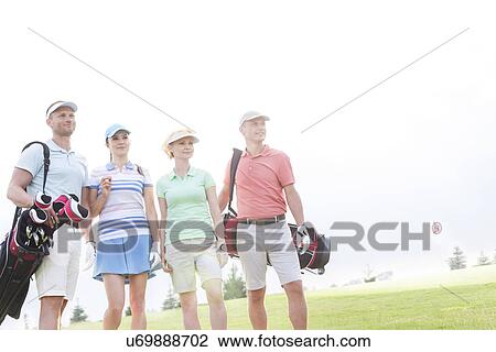 Male and female friends standing at golf course against clear sky View Large Photo Image Stock Image - Male and female friends standing at golf course against clear sky. Fotosearch