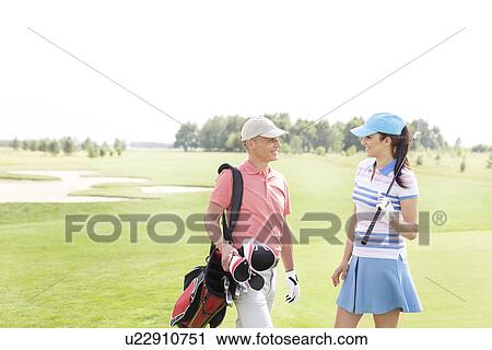 Stock Image - Male and female golfers communicating at golf course. Fotosearch