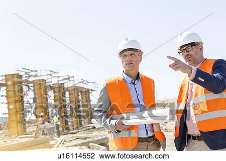 Male engineers discussing at construction site against clear sky View Large Photo Image Stock Image - Male engineers discussing at construction site against clear sky. Fotosearch