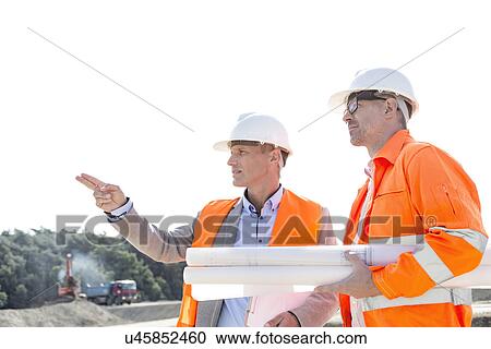 Male engineers discussing at construction site against clear sky View Large Photo Image Stock Image - Male engineers discussing at construction site against clear sky. Fotosearch
