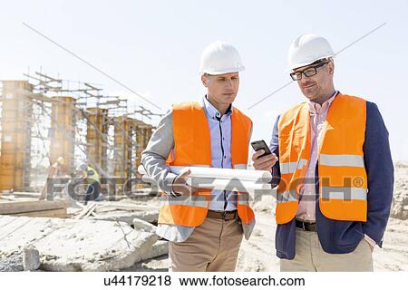 Stock Photo - Male engineers using mobile phone at construction site against clear sky. Fotosearch