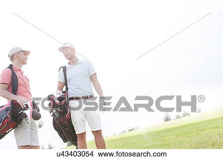 Picture - Male friends conversing at golf course against clear sky on sunny day. Fotosearch