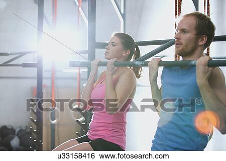 Man and woman doing pull ups in crossfit gym View Large Photo Image Stock Photograph - Man and woman doing pull ups in crossfit gym. Fotosearch