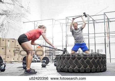 Man and woman hitting tire with sledgehammer in crossfit gym View Large Photo Image Stock Photograph - Man and woman hitting tire with sledgehammer in crossfit gym. Fotosearch