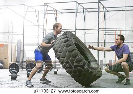 Man assisting at dedicated friend in flipping tire at crossfit gym View Large Photo Image Stock Photo - Man assisting at dedicated friend in flipping tire at crossfit gym. Fotosearch