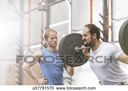 Man assisting friend in lifting barbell at crossfit gym View Large Photo Image Stock Image - Man assisting friend in lifting barbell at crossfit gym. Fotosearch
