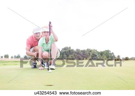 Man assisting woman aiming ball on golf course against clear sky View Large Photo Image Stock Image - Man assisting woman aiming ball on golf course against clear sky. Fotosearch