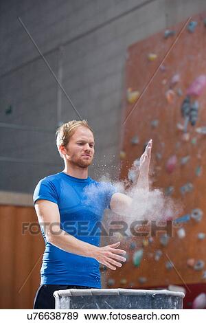 Stock Photo - Man dusting powder by climbing wall in crossfit gym. Fotosearch