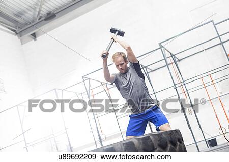 Man hitting tire with sledgehammer in crossfit gym View Large Photo Image Stock Photo - Man hitting tire with sledgehammer in crossfit gym. Fotosearch