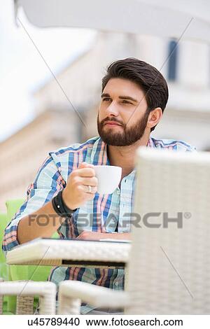 Stock Image - Man looking away while having coffee at sidewalk cafe. Fotosearch
