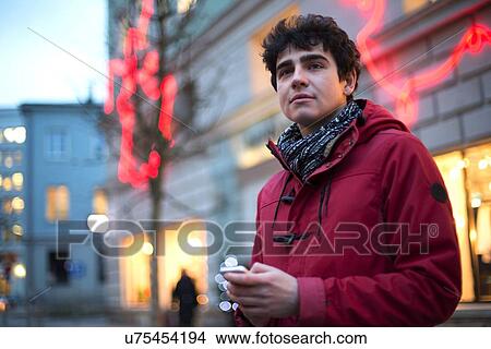 Man looking away while holding cell phone in city during winter View Large Photo Image Picture - Man looking away while holding cell phone in city during winter. Fotosearch