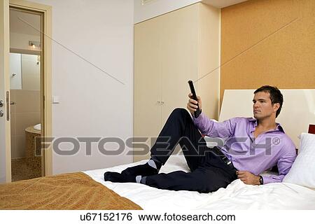 Stock Photograph - Man on bed with remote control. Fotosearch