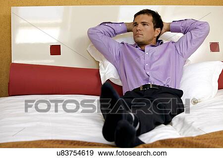 Man relaxing in hotel room with hands behind head View Large Photo Image Stock Photo - Man relaxing in hotel room with hands behind head. Fotosearch