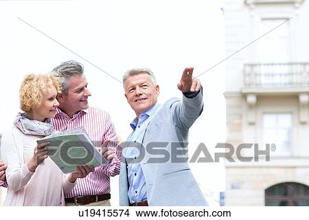 Man showing direction to couple with road map in city View Large Photo Image Picture - Man showing direction to couple with road map in city. Fotosearch