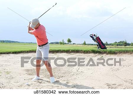 Stock Image - Man swinging at golf course against sky. Fotosearch