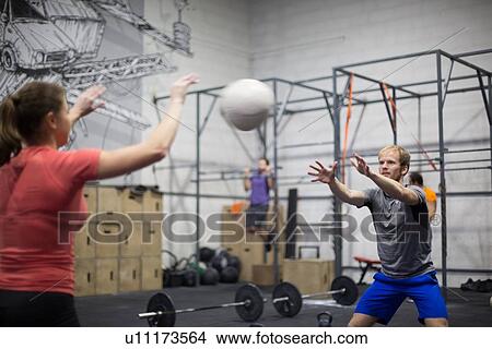 Man throwing medicine ball towards woman in crossfit gym View Large Photo Image Picture - Man throwing medicine ball towards woman in crossfit gym. Fotosearch