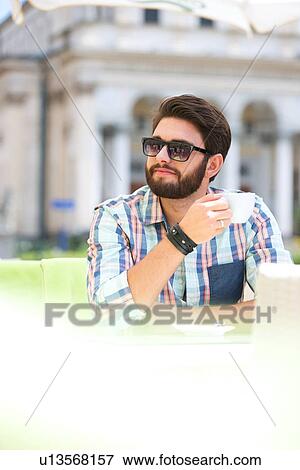 Stock Photo - Mid-adult man looking away while having coffee at sidewalk cafe. Fotosearch