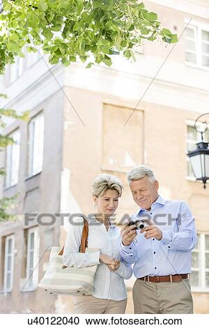 Middle-aged couple reviewing photos on digital camera outside building View Large Photo Image Stock Image - Middle-aged couple reviewing photos on digital camera outside building. Fotosearch