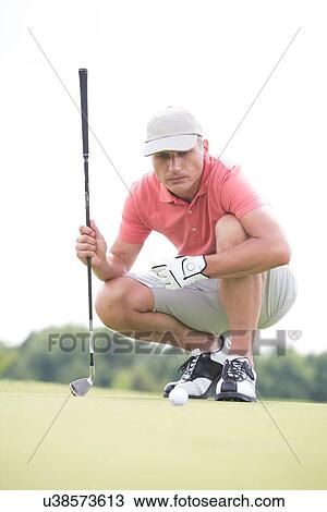 Middle-aged man aiming ball while crouching on golf course View Large Photo Image Stock Image - Middle-aged man aiming ball while crouching on golf course. Fotosearch