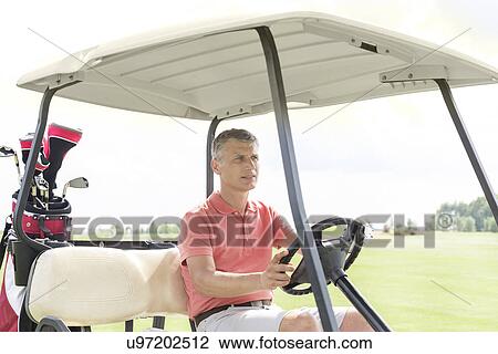 Stock Image - Middle-aged man driving cart at golf course. Fotosearch