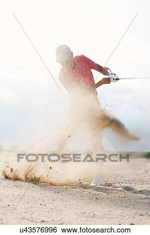 Stock Photograph - Middle-aged man splashing sand while playing at golf course. Fotosearch