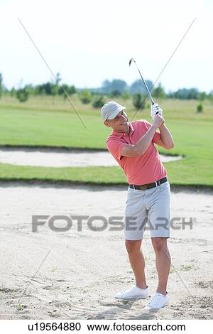Stock Image - Middle-aged man swinging at golf course. Fotosearch