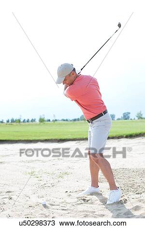 Stock Image - Middle-aged man swinging at golf course against clear sky. Fotosearch