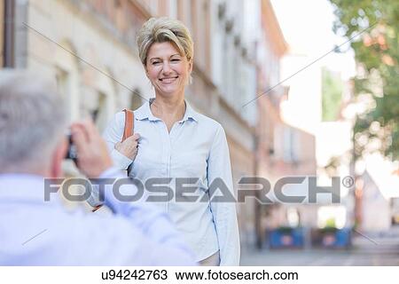 Stock Image - Middle-aged man taking picture of woman in city. Fotosearch