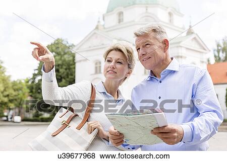 Stock Photo - Middle-aged woman showing something to man holding map outdoors. Fotosearch