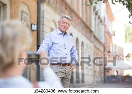 Stock Photograph - Middle-aged woman taking picture of man in city. Fotosearch