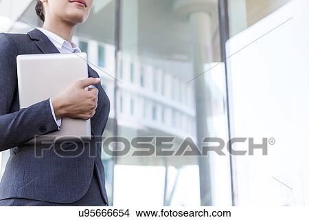 Midsection of businesswoman holding tablet PC by glass wall View Large Photo Image Picture - Midsection of businesswoman holding tablet PC by glass wall. Fotosearch