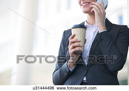 Midsection of businesswoman using cell phone while holding disposable cup outdoors View Large Photo Image Stock Photograph - Midsection of businesswoman using cell phone while holding disposable cup outdoors. Fotosearch