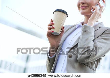 Stock Photography - Midsection of businesswoman using cell phone while holding disposable cup outdoors. Fotosearch