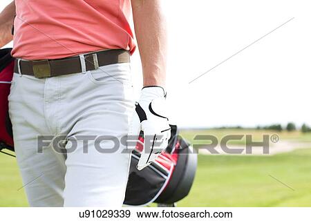Stock Photo - Midsection of man carrying golf club bag while walking at course. Fotosearch