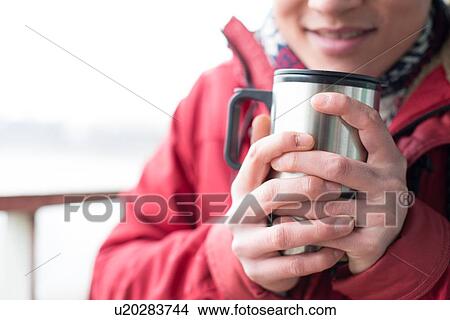 Picture - Midsection of man holding insulated drink container during winter. Fotosearch