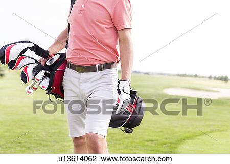 Stock Image - Midsection of man with golf club bag standing at course. Fotosearch
