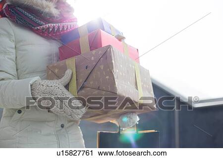 Stock Image - Midsection of woman carrying stacked gifts during winter by window. Fotosearch