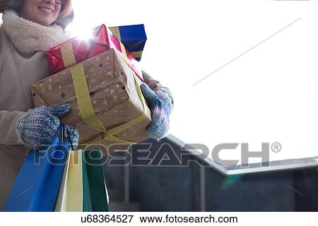 Stock Photo - Midsection of woman with stacked gifts and shopping standing by window during winter. Fotosearch