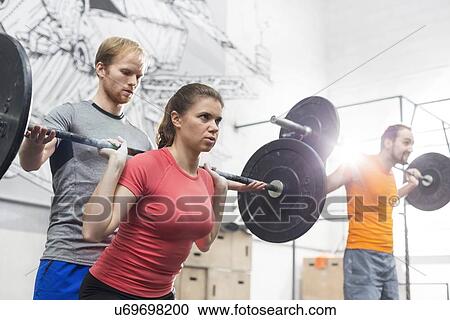 Stock Image - People lifting barbells in crossfit gym. Fotosearch