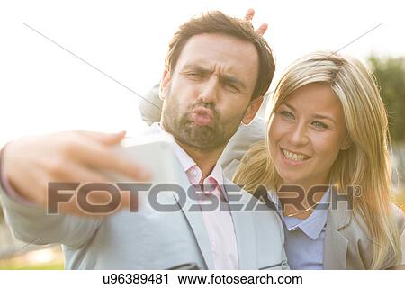 Stock Image - Playful business couple taking selfie outdoors on sunny day. Fotosearch