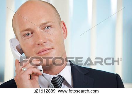 Stock Photo - Portrait of businessman talking on telephone at office. Fotosearch