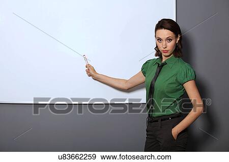 Stock Photo - Portrait of businesswoman with hands in pockets pointing at whiteboard in office. Fotosearch