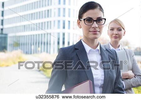 Stock Photograph - Portrait of confident businesswoman with colleague in background. Fotosearch