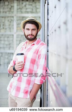 Stock Photo - Portrait of confident man holding disposable cup while leaning on wall. Fotosearch