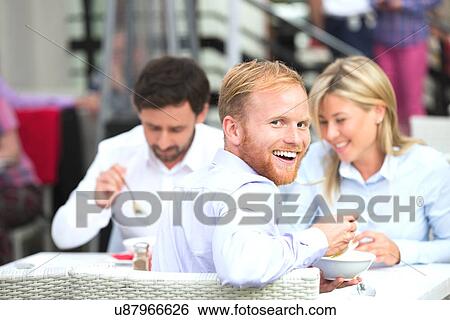 Stock Photograph - Portrait of happy businessman sitting with colleagues at outdoor restaurant. Fotosearch