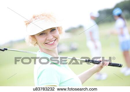 Stock Image - Portrait of happy female golfer holding golf club. Fotosearch