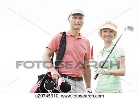 Stock Image - Portrait of happy male and female golfers standing against clear sky. Fotosearch