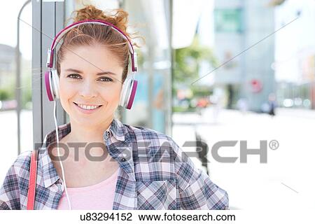 Portrait of happy woman wearing headphones while waiting at bus stop View Large Photo Image Stock Image - Portrait of happy woman wearing headphones while waiting at bus stop. Fotosearch