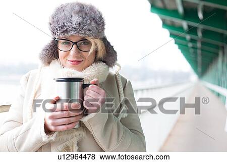 Stock Photo - Portrait of smiling woman in warm clothing holding insulated drink container. Fotosearch